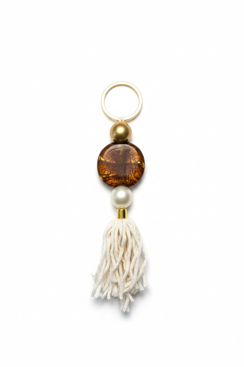 Keychain with brown bead, pearl, and white tassel on a beige background