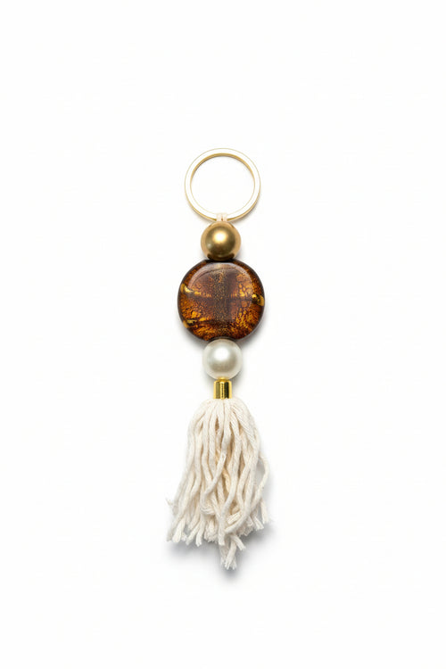 Keychain with brown bead, pearl, and white tassel on a beige background