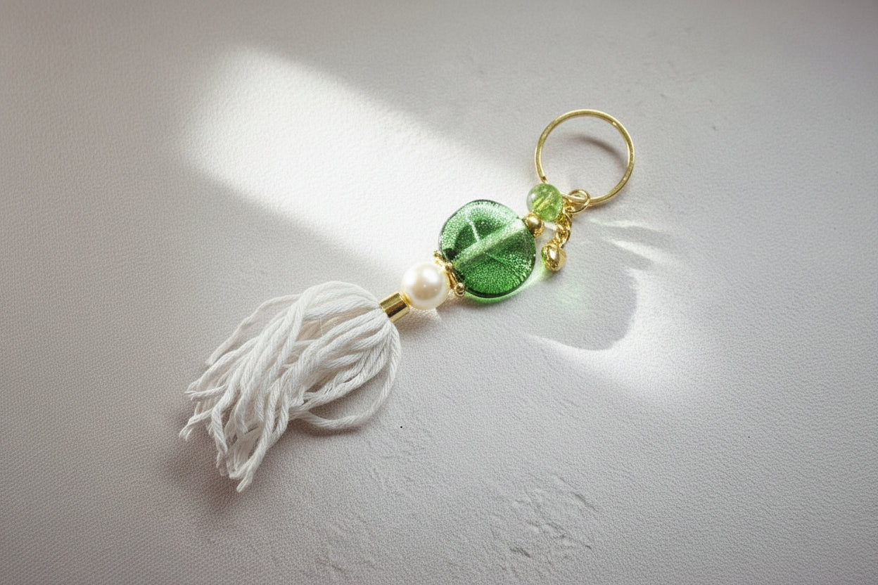Keychain with green leaf charm, pearl, and white tassel on a gray background