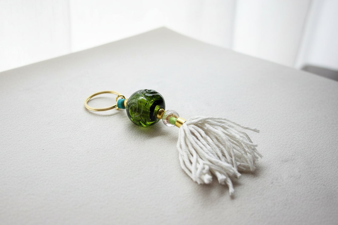 Keychain with green bead and white tassel on a gray background